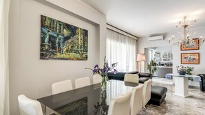 Een moderne woonkamer met een eethoek, een kroonluchter en kunstwerken aan de muur.