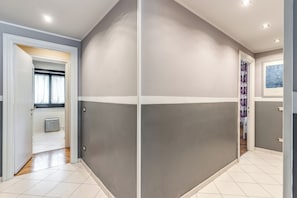 Un pasillo con pared blanca y gris, una puerta que da a un baño y una ventana con cortinas.