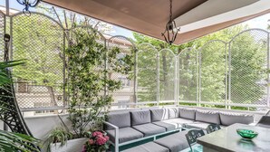 Een overdekt terras met een comfortabele bank, een tafel en een plant in pot.