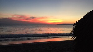 Une plage au coucher du soleil, avec des vagues et une structure recouverte de chaume.