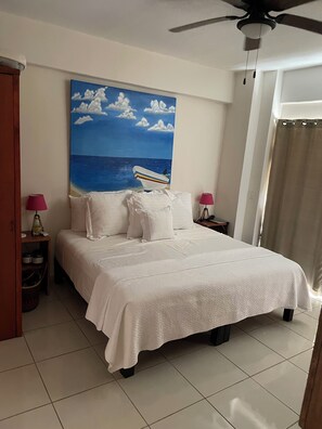 A bedroom with a bed, a ceiling fan, a painting of a boat on the sea, and a nightstand with a lamp. - Rare, 1 Bedroom Condo in the Marina, Pool, Marina Boardwalk and Golf Course (Puerto vallarta)