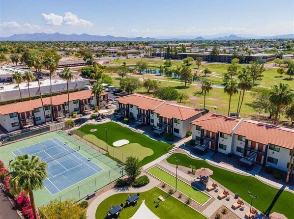 A hotel with multiple-story buildings, a tennis court, and a landscaped area with palm trees.