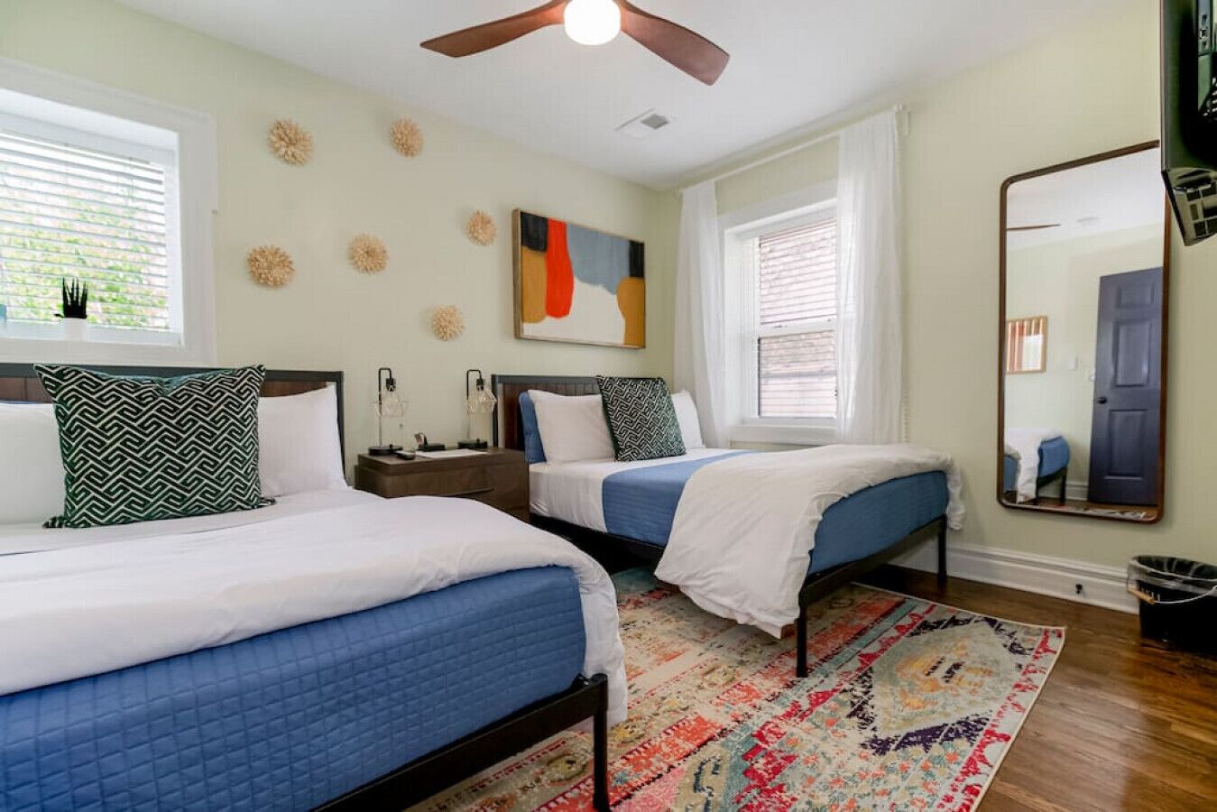 A hotel room with two beds, a ceiling fan, a large mirror, and a colorful rug.