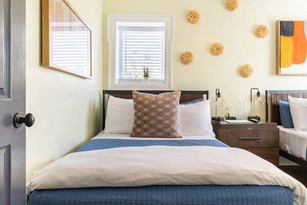 A neatly made bed with a blue and white duvet, a bedside table with a lamp, and a wall decorated with geometric wall art.