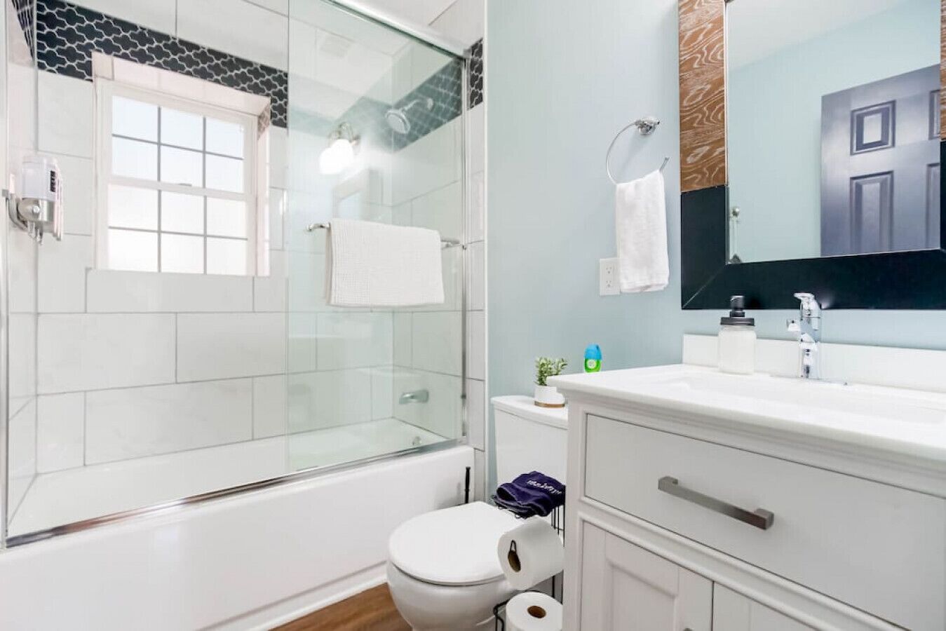 A modern bathroom with a glass-enclosed shower, white tiles, a toilet, and a vanity with a mirror.