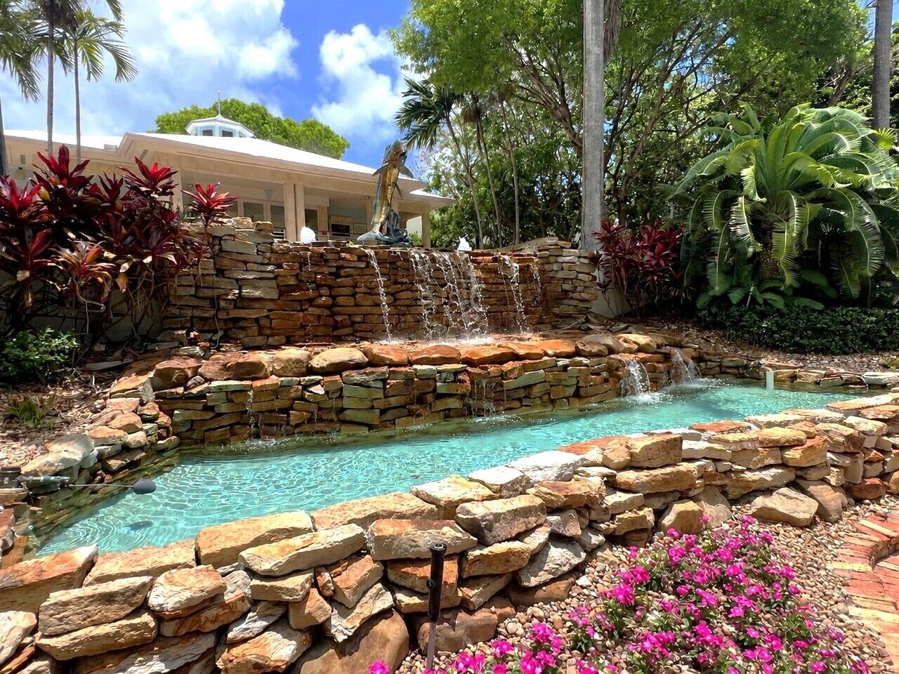 Una piscina con cascada, rodeada de muros de piedra y plantas tropicales.
