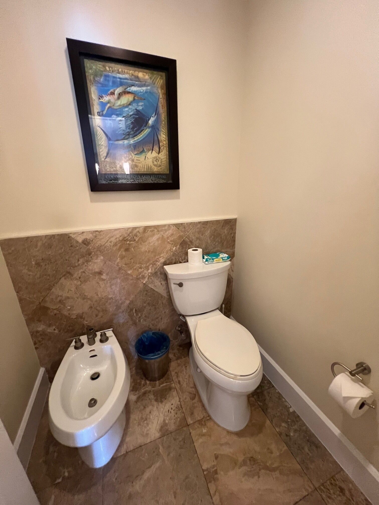 A bathroom with a toilet, bidet, marble floor, and a framed picture on the wall.