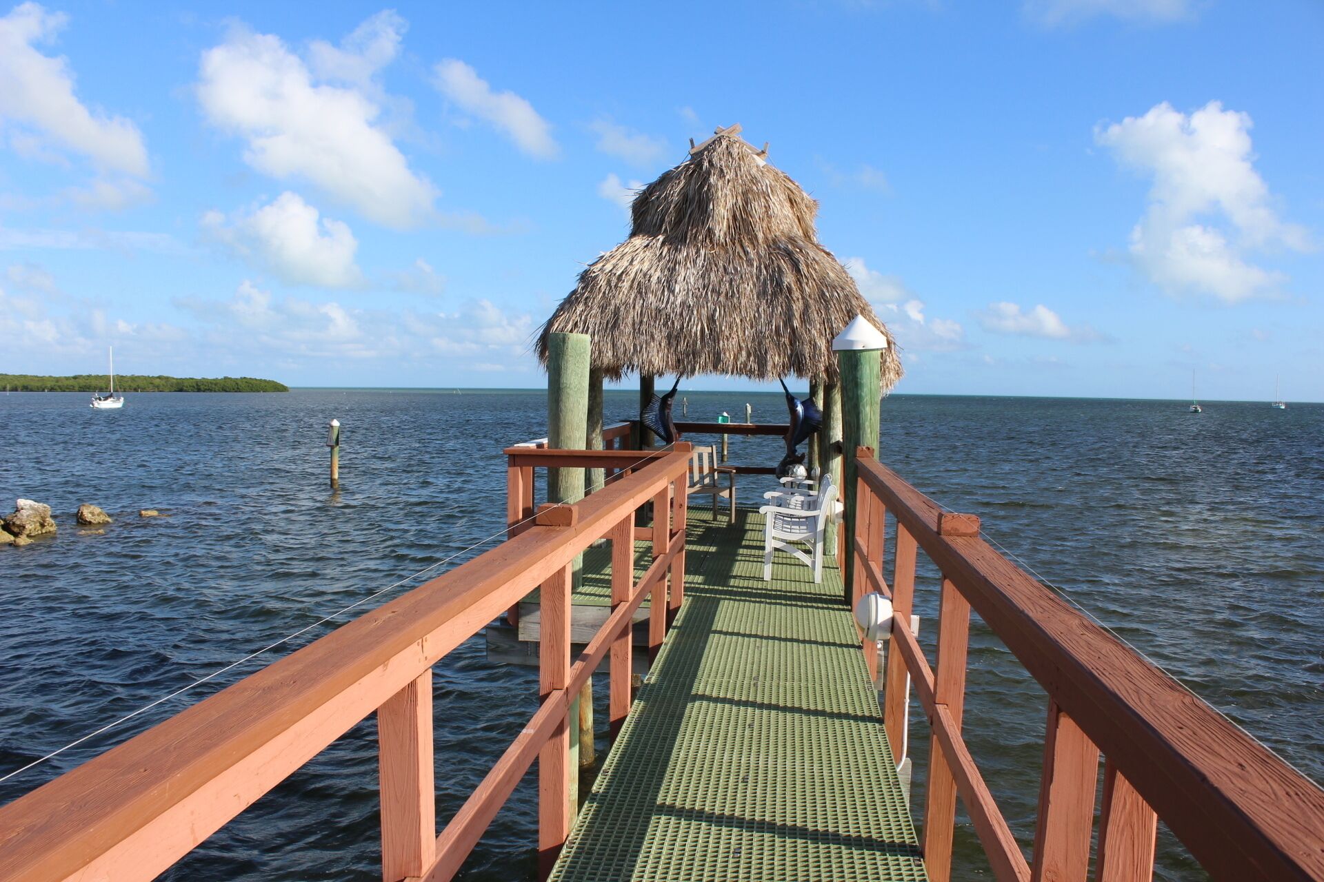A wooden pier leading to a thatched-roof structure with a view of the sea and distant land.