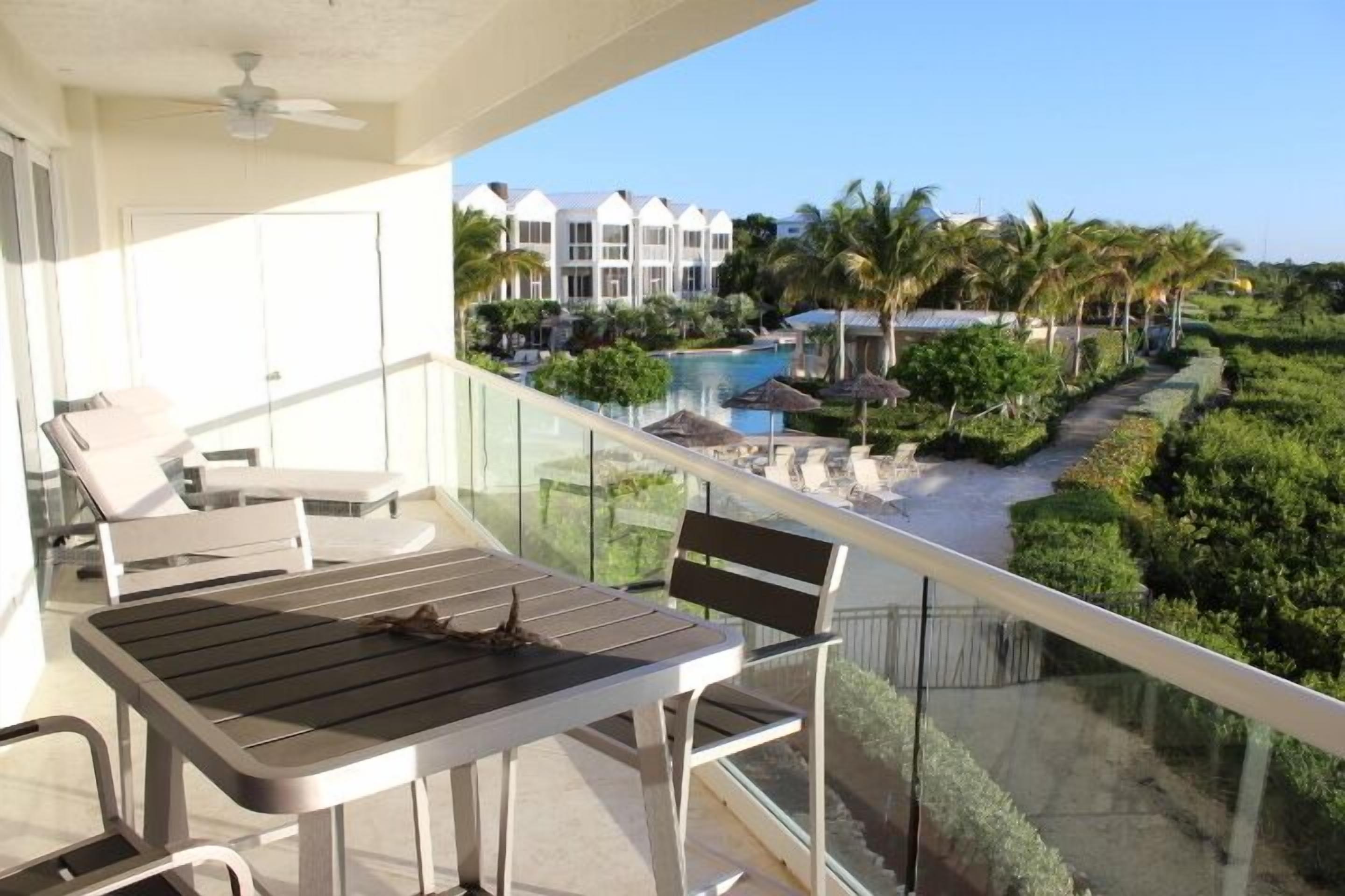 A balcony with a table and chairs, overlooking a pool and resort buildings.