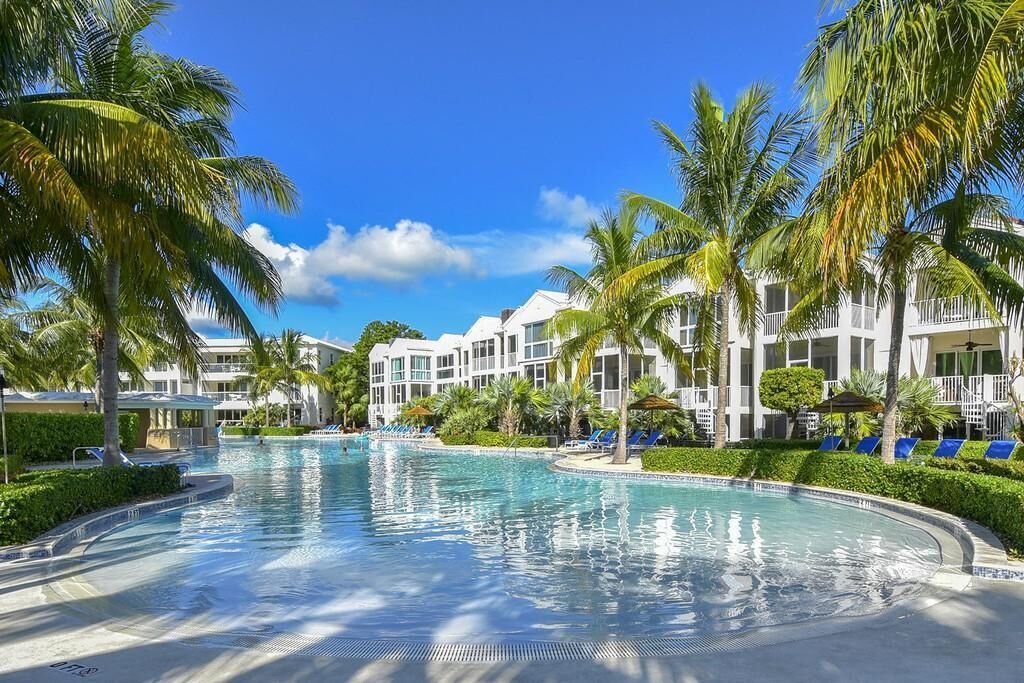 A resort with a swimming pool surrounded by palm trees and a building with balconies.