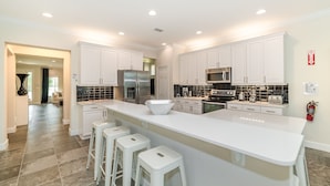 A modern kitchen with white cabinets, stainless steel appliances, and a large island with bar stools. - 🏡✨ Luxurious Model Resort Pool Home Near Disney! Perfect for Family Fun! (kissimmee)