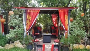 A covered outdoor seating area with red curtains and a table with a candle. - Beautiful 5 rm.Hardwood Austin Home! (Austin)
