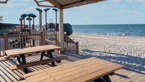 Een houten terras met picknicktafels met uitzicht op een strand.
