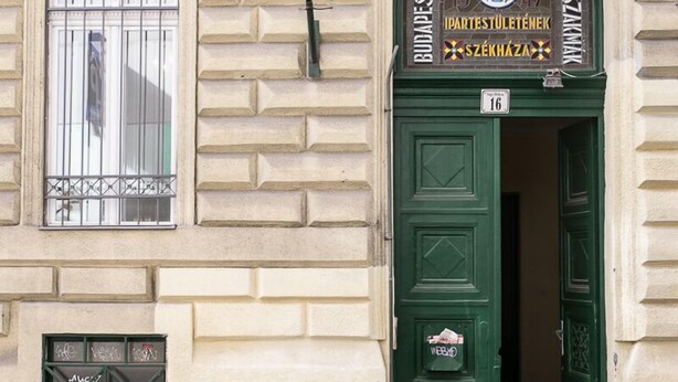 Un edificio con un ingresso ad arco verde, una targa sopra la porta e una finestra con grate.