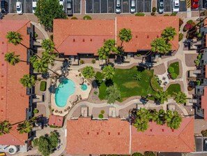 Vue aérienne d’un quartier résidentiel avec une piscine, des palmiers et un parking.
