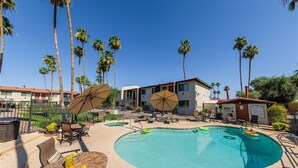 A swimming pool with lounge chairs and umbrellas, surrounded by palm trees and a building with a red roof. - 240 Relaxing Scottsdale Stay – Pet-Friendly, Park Views & Putting Green (Scottsdale)