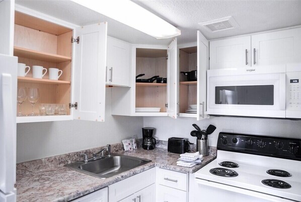 A compact kitchen with white cabinets, a built-in microwave, a stove, and a sink. - 240 Relaxing Scottsdale Stay – Pet-Friendly, Park Views & Putting Green (Scottsdale)