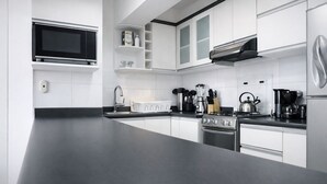 Une cuisine moderne avec des meubles blancs, un plan de travail noir, une cuisinière, un four à micro-ondes et une machine à café.