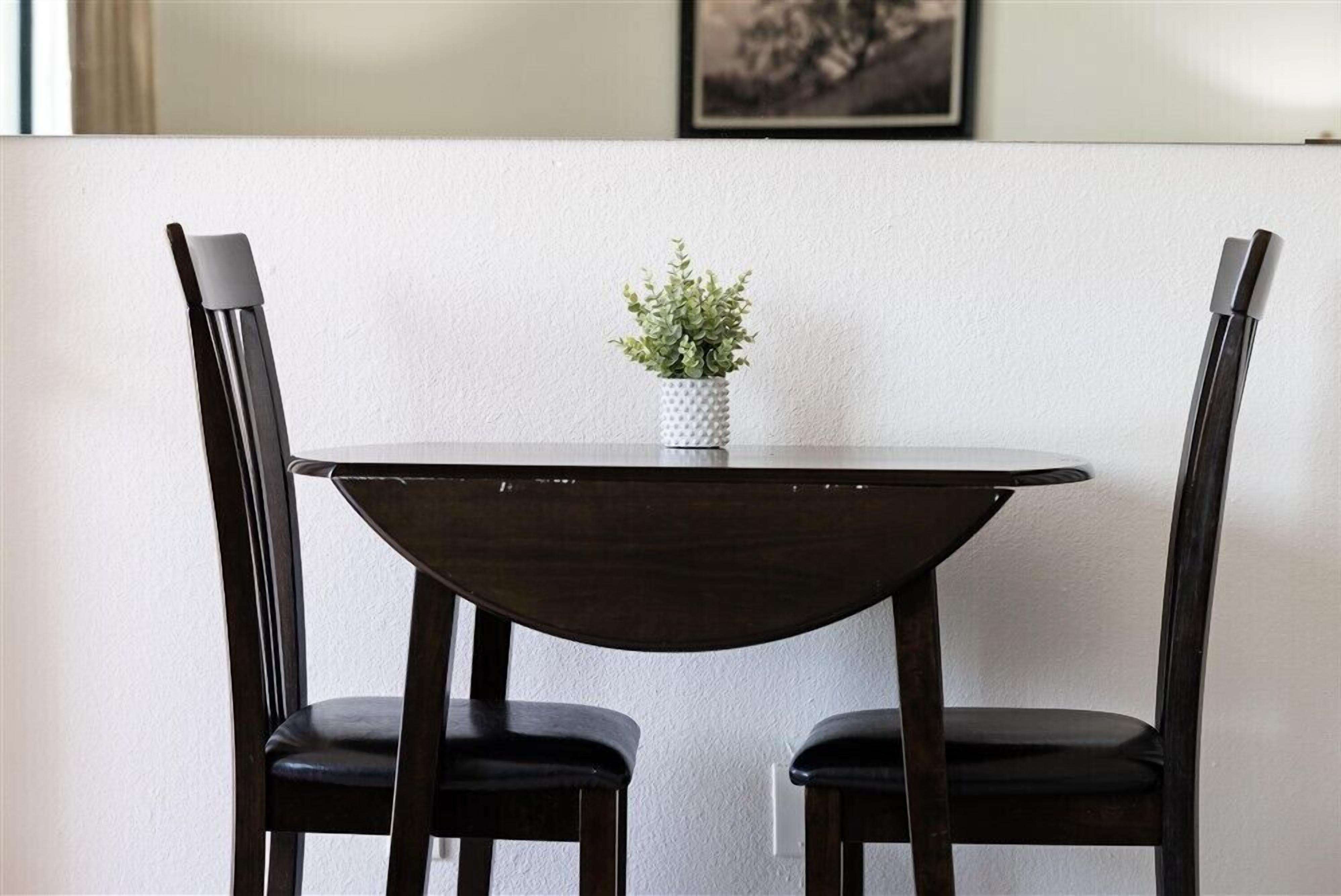 Una mesa de comedor con dos sillas, una planta pequeña en maceta y un cuadro en la pared.