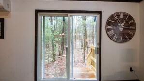 A room with a large wooden clock on the wall, a sliding glass door leading to a wooden deck, and a small table with a blue mat.