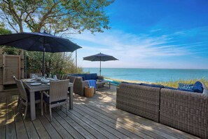 Een houten terras met rieten meubels, een tafel gedekt met borden en glazen, en twee parasols die schaduw bieden.
