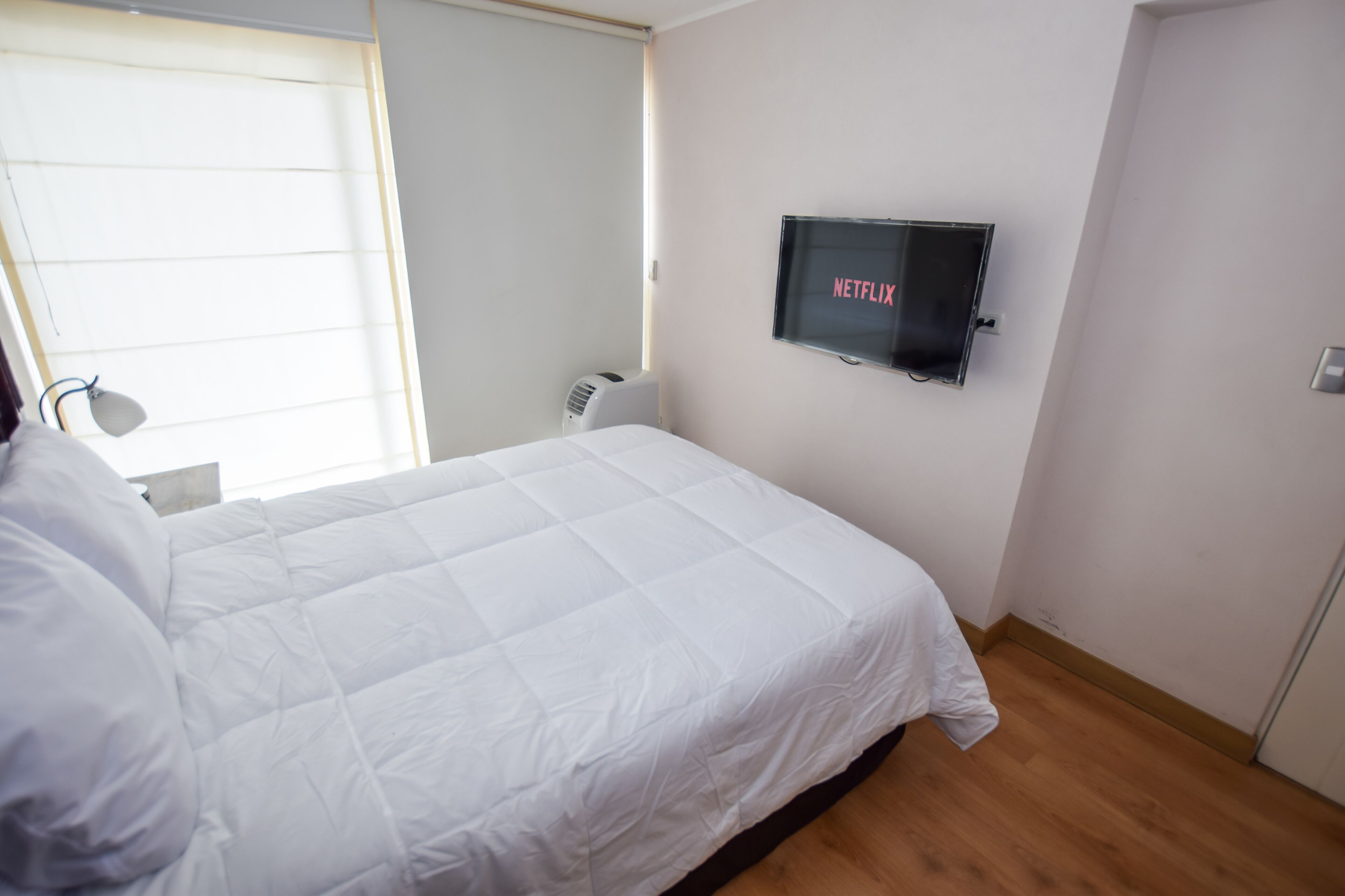 A bedroom with a bed, a wall-mounted TV, a window, and a radiator.
