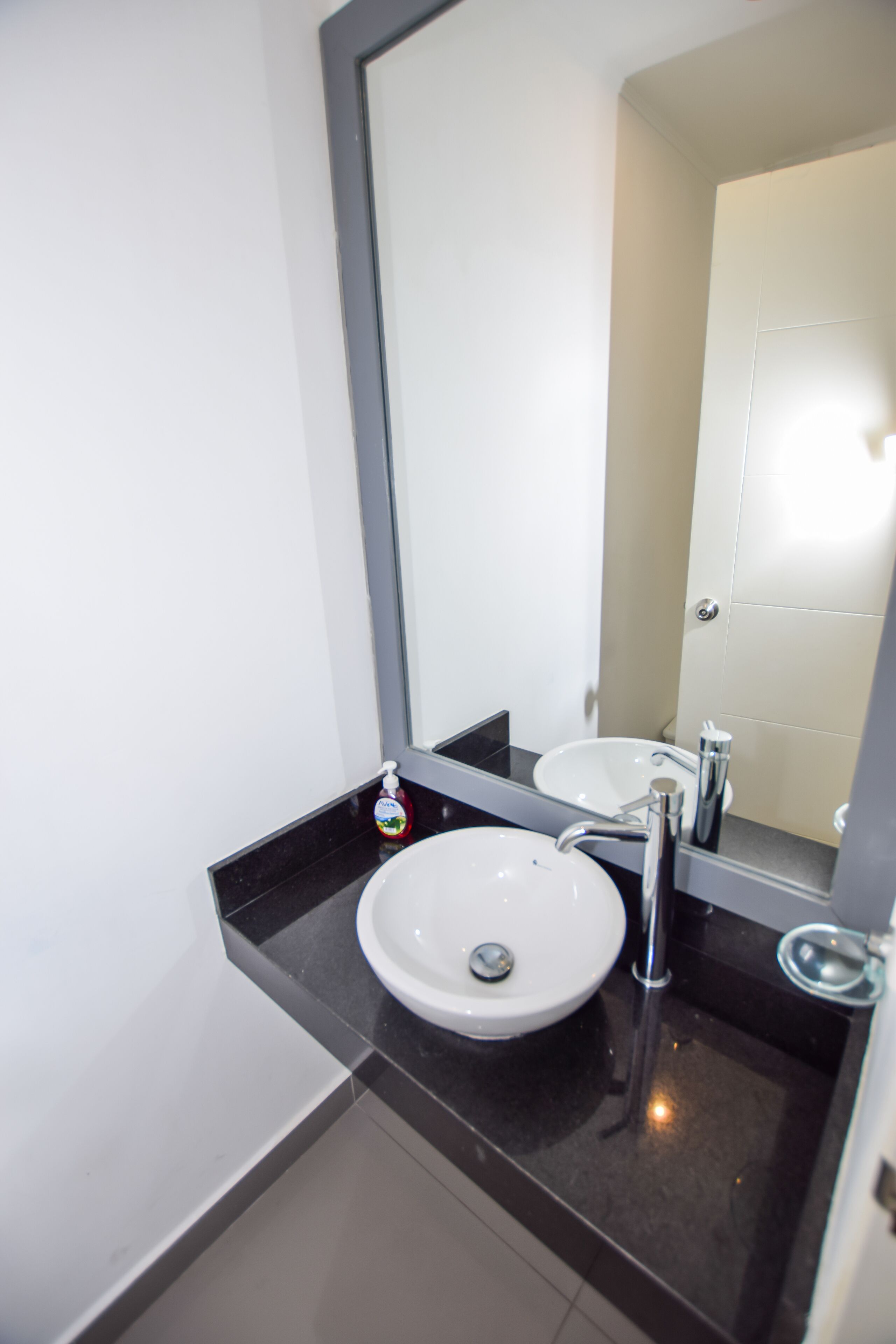 Une salle de bain moderne avec un lavabo blanc, un grand miroir et un plan de toilette noir.