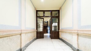 A corridor with tiled flooring, wooden doors, and a staircase in the background.