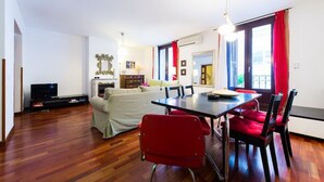 A modern living room with a sofa, TV, and dining area with chairs and a table.