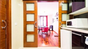 A kitchen with a microwave and cabinets, a dining area with red chairs, and a wooden door with frosted glass panels.