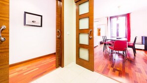 A hallway with wooden flooring leading to a dining area with red chairs and a table.