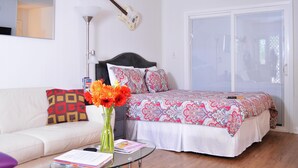 Quarto com cama, mesa de cabeceira, abajur, violão e janela.