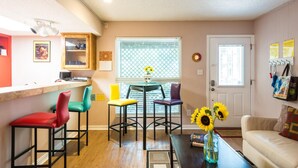 Um espaço compacto com cozinha, mesa de jantar com cadeiras coloridas, sofá e mesa de centro com um vaso de girassóis.