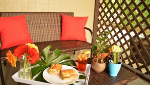 Uma mesa de vime com uma bandeja contendo um sanduíche, um copo de chá gelado e um vaso de flores.