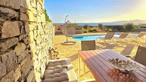 Eine Steinsäule, ein Holztisch, ein Pool und Liegestühle.