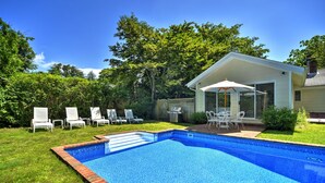 A backyard with a swimming pool, a patio with chairs, and a covered seating area. - Stylish East Hampton Village Retreat- Heated Pool and Sauna, Steps to Village (East Hampton)