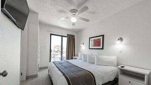 Een hotelkamer met een bed, nachtkastje, plafondventilator, televisie en raam met gordijnen.