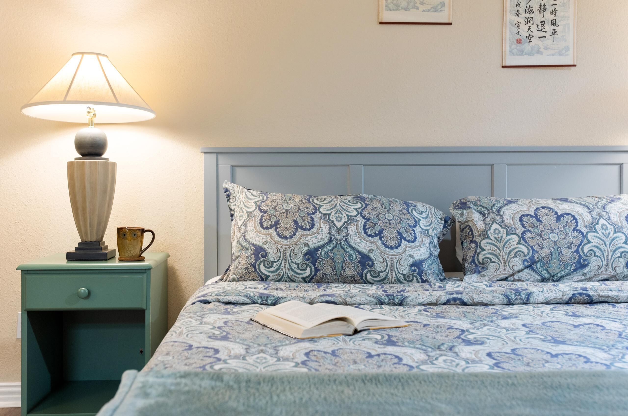 A bedroom with a bed, a nightstand, a lamp, and a book.