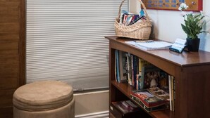 Une pièce avec une fenêtre, un bureau en bois avec des livres, un panier et un miroir.
