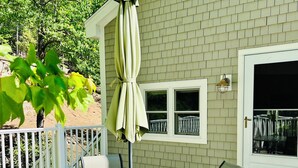 A covered patio with a round glass table and four chairs, a green umbrella, and a white door with windows.