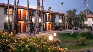 A multi-story motel with a red-tiled roof, multiple balconies, and a landscaped garden with palm trees and flowers. - 218 Scottsdale Charmer: Pool, Patio, and Perfectly Located (Scottsdale)