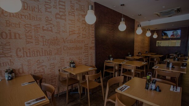 Interior de restaurante con mesas y sillas de madera, luminarias y una pared con palabras relacionadas con la comida.