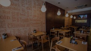 Et restaurantmiljø med træborde og stole, lamper og en væg med ord relateret til mad.