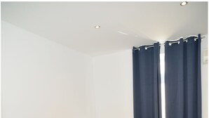 Habitación de hotel con dos camas individuales, cabecera de madera, mesita de noche con lámpara y cortinas oscuras.