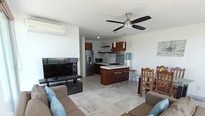 A living room with a TV, sofa, and a dining area with chairs and a table.