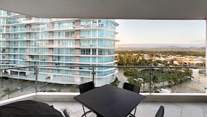 A balcony with a table and chairs, overlooking a modern building and a cityscape.