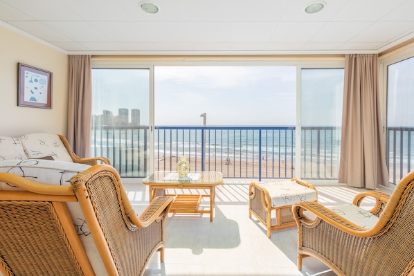 A balcony with wicker furniture, a glass table, and a view of the beach and ocean.