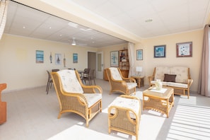 A spacious living room with wicker furniture, a dining area, and a bookshelf.