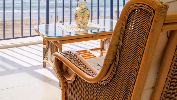 A balcony with a wicker chair, a glass table, and a decorative vase. - ApartUP Acapulco Beachfront Views (Oropesa del Mar)