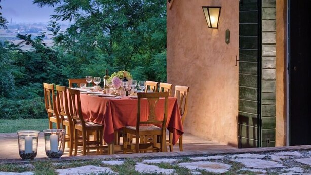 An outdoor dining area with a table set for four, surrounded by chairs, under a wooden pergola with a view of the night sky and trees.